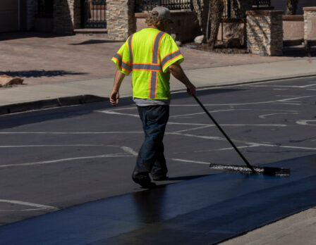 Worker using a sealcoating brush during asphalt resurfacing project
